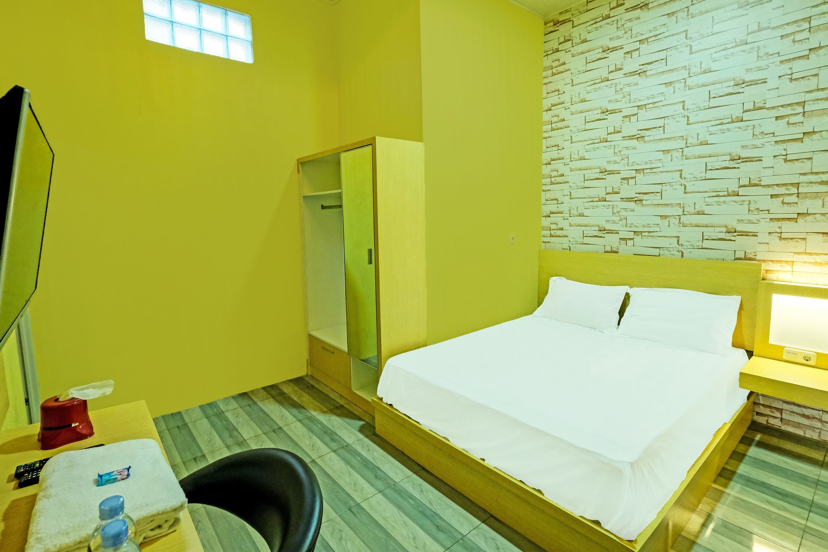 A hotel room with a bed, a desk with a chair, a wardrobe, and a small window.