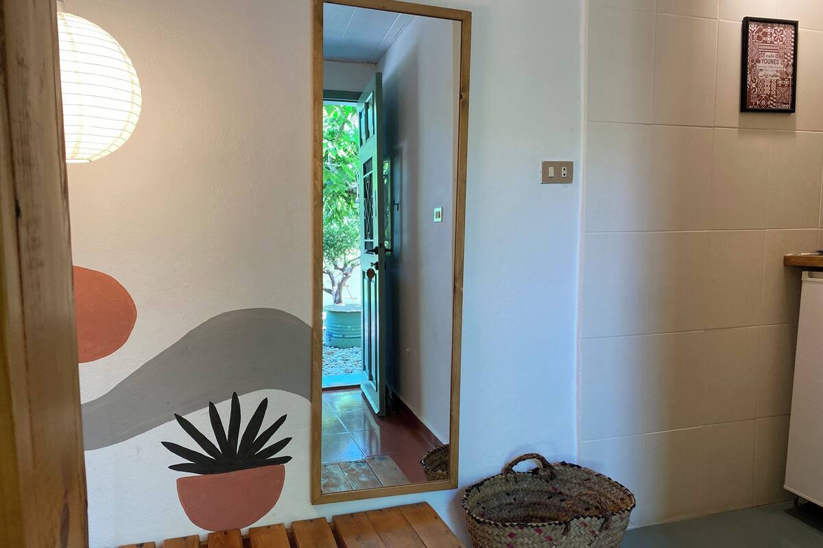Um corredor com um banco de madeira, uma cesta de vime, um espelho e um painel com um desenho circular e uma moldura com uma imagem.