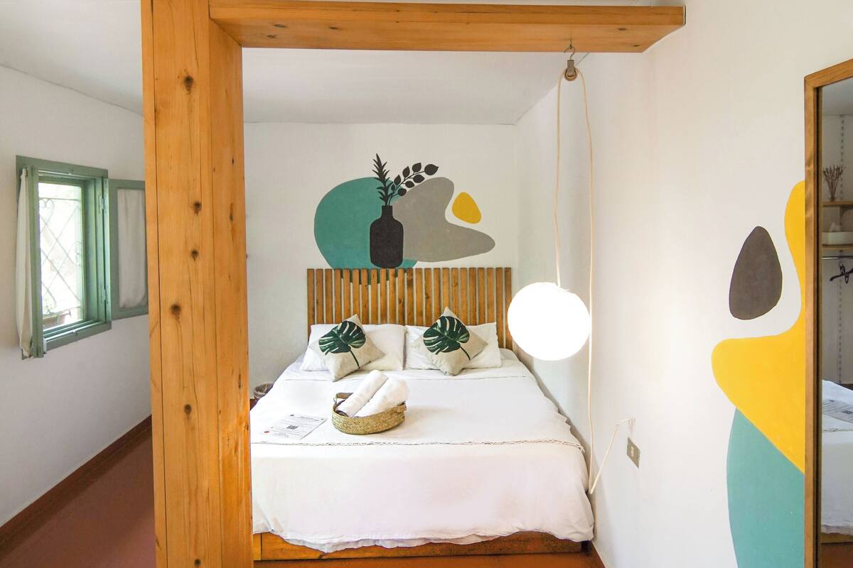 Quarto com estrutura de cama em madeira, luminária de cabeceira e parede com arte abstrata.