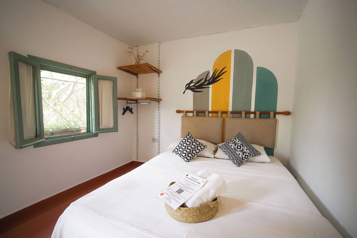 Uma cama bem arrumada com cabeceira, uma mesa de cabeceira com um vaso e uma janela com cortinas.