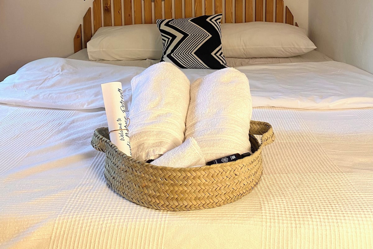 Cama bem arrumada com uma cesta de tecido contendo toalhas e um cartão de boas-vindas enrolado.