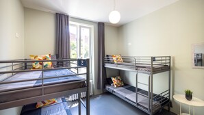 Un dormitorio con literas, una mesita con una planta y una ventana con cortinas.