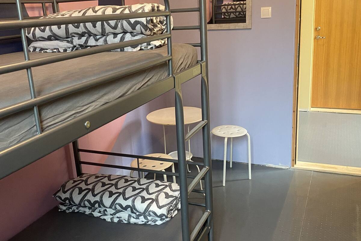 A bunk bed with patterned pillows, a small round table, and a door with a number.