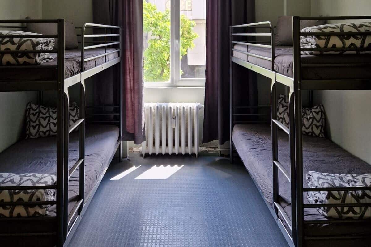 A dormitory room with bunk beds, a window with curtains, and a radiator.