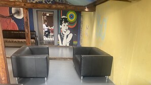 Un área de descanso con sillas negras acolchadas y un suelo estampado, un mural con diseño de diana y una pared amarilla con grafitis.