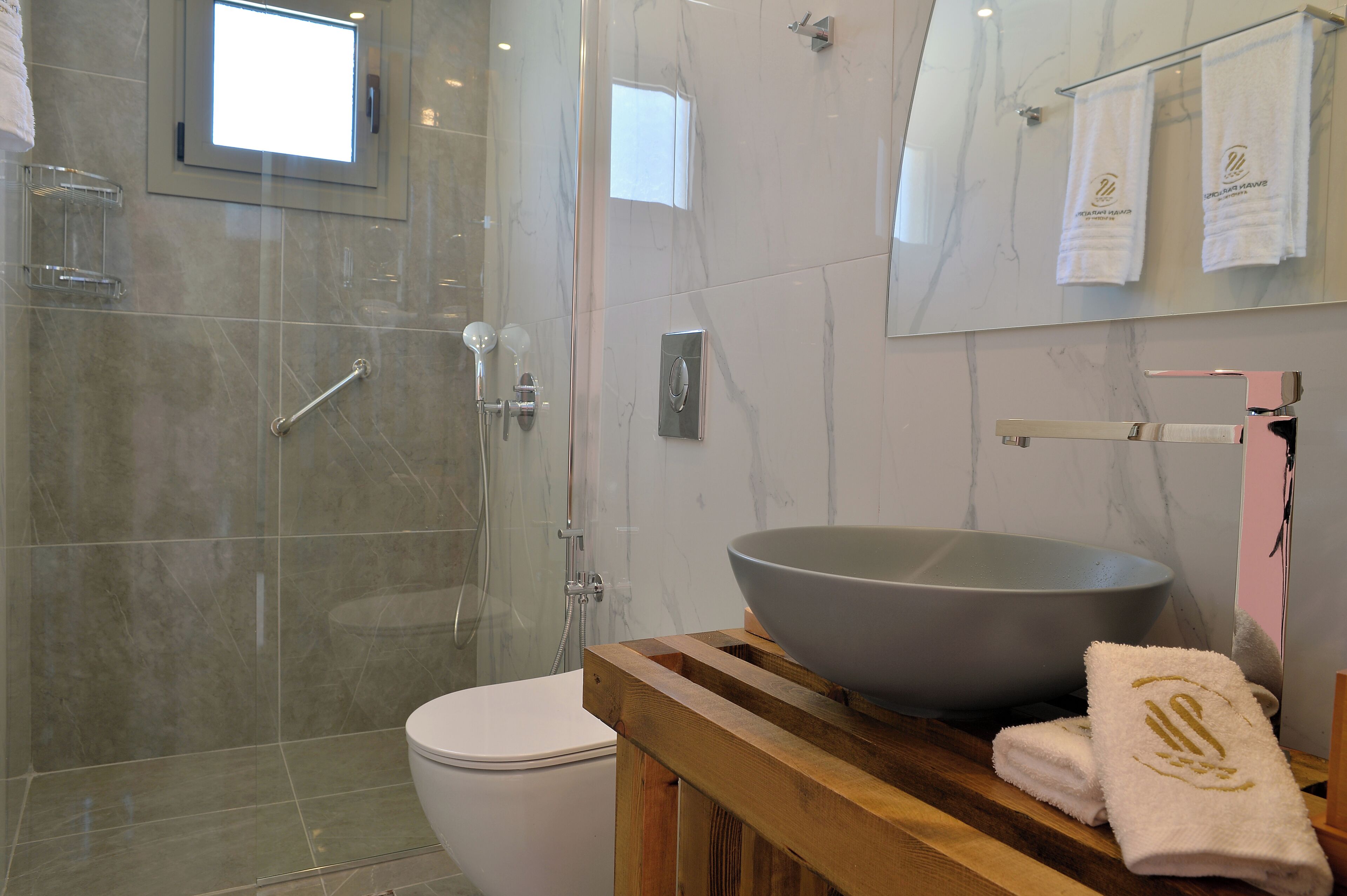 Un baño moderno con ducha envuelta en vidrio, inodoro blanco y tocador de madera con un lavabo grande.