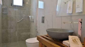 Un baño moderno con ducha envuelta en vidrio, inodoro blanco y tocador de madera con un lavabo grande.