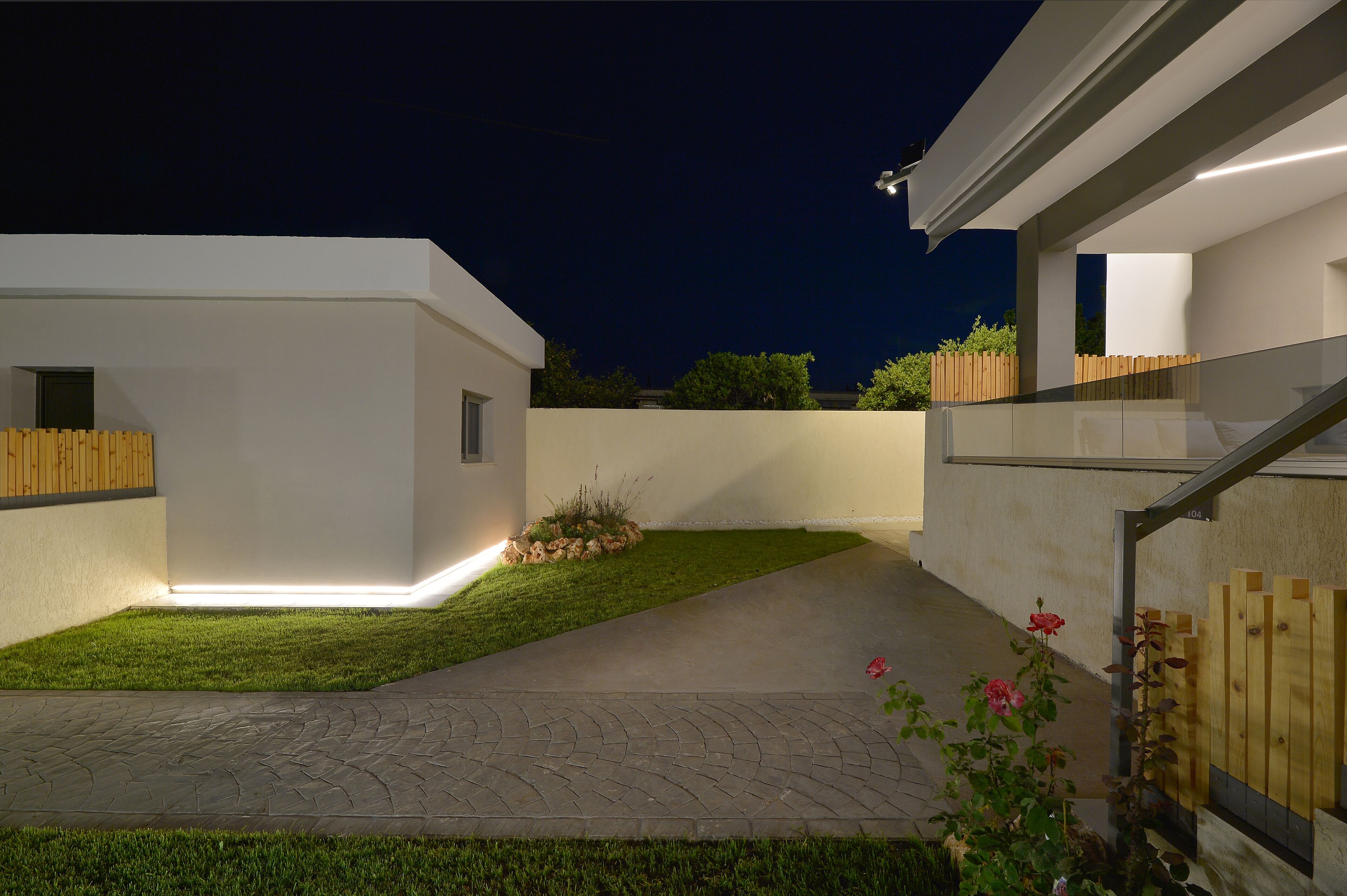 A modern residential exterior with a paved driveway, a small lawn, and a wooden fence.