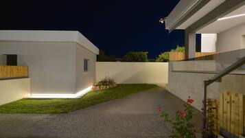 A modern residential exterior with a paved driveway, a small lawn, and a wooden fence.