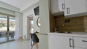 Una cuina moderna amb armaris blancs, un rentapeus d'acer inoxidable i vista a l'exterior a través d'una porta corredissa de vidre.
