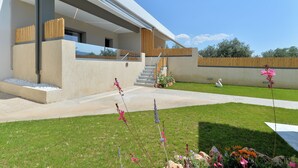 Una casa moderna amb un porxo cobert, una escala visible i un jardí ben cuidat amb flors.