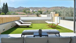 Un pati exterior modern amb zona enjardinada, seients de relax i una taula amb un ramader ornamental.