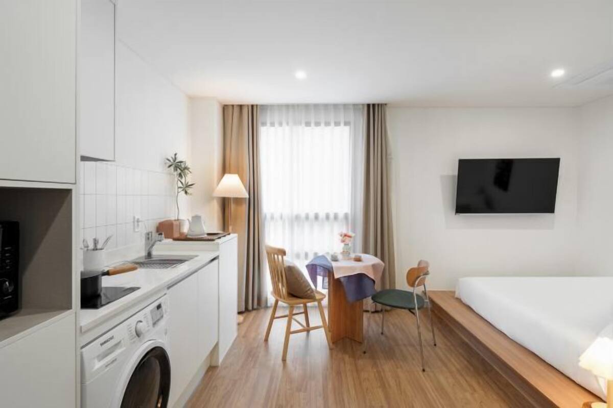 Una habitación de hotel con kitchenette, comedor, cama y televisor montado en la pared.