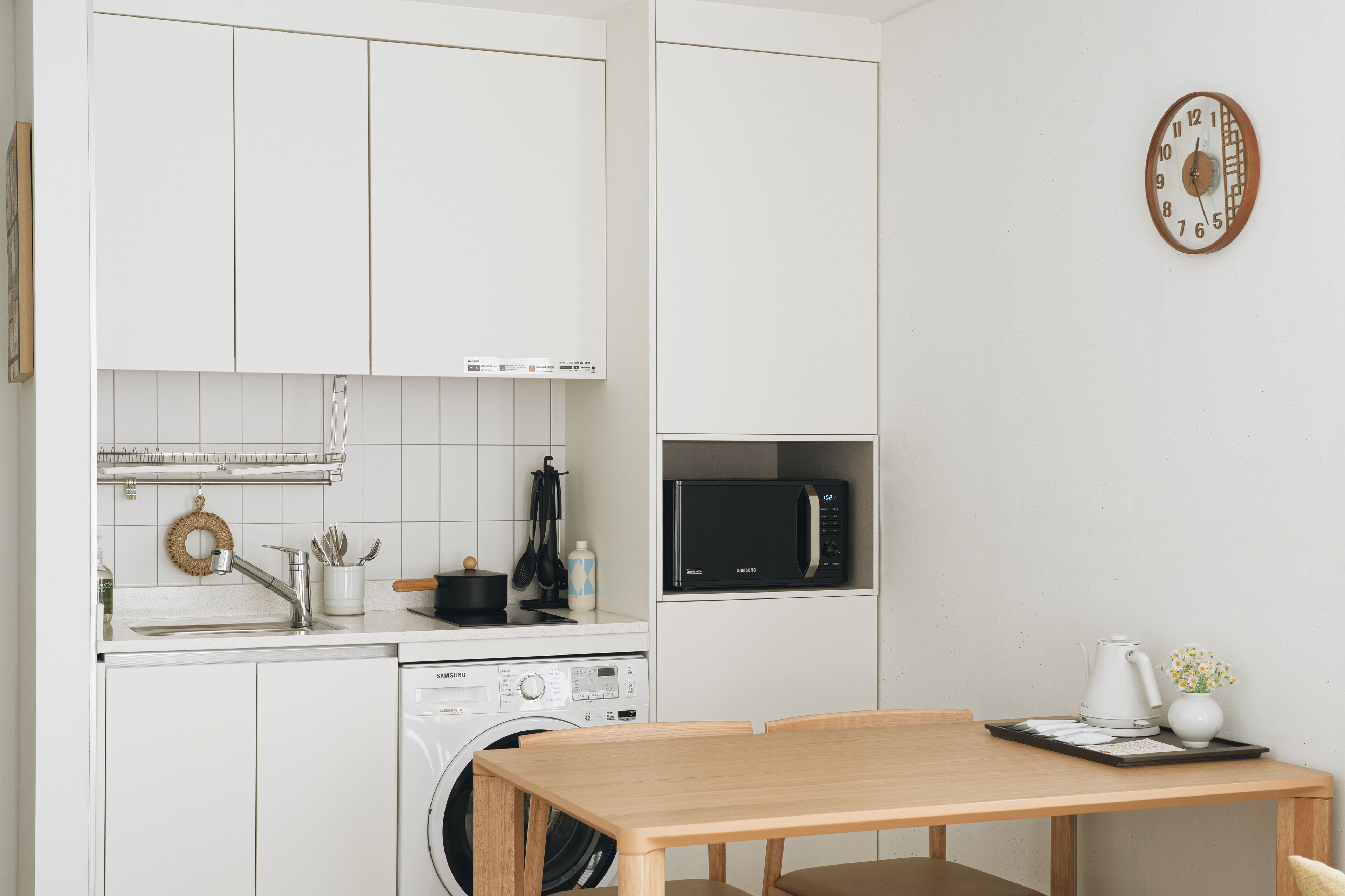 Una cocina compacta con muebles blancos, un microondas, una lavadora y una mesa de comedor.