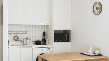 Una cocina compacta con muebles blancos, un microondas, una lavadora y una mesa de comedor.