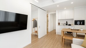 Una cocina moderna con armarios blancos, una mesa de comedor de madera y un televisor de pantalla plana montado en la pared.