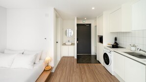 Habitación de hotel moderna con cama, mesita de noche, lámpara y vistas al pasillo que conduce a la cocina.