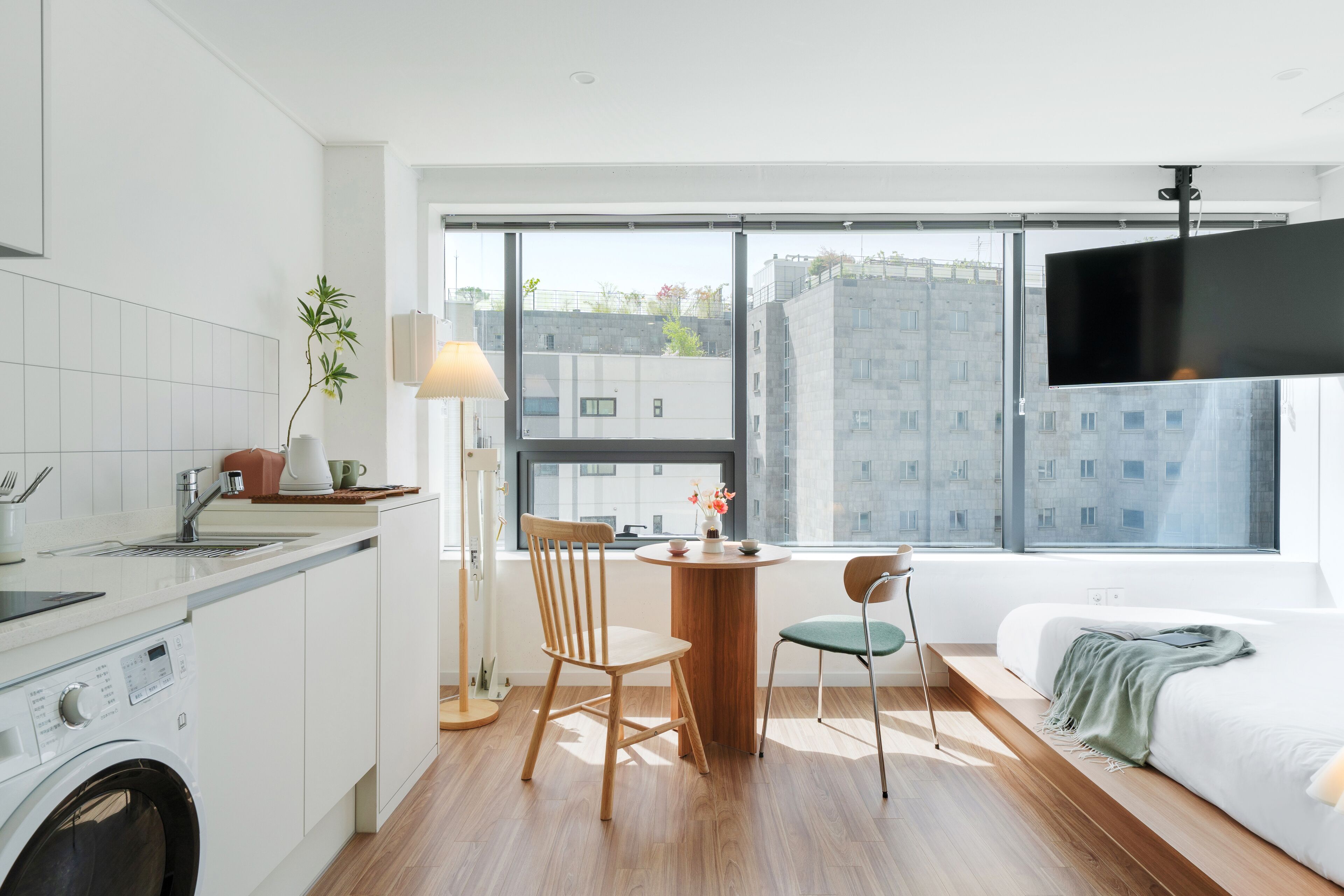 Una cocina moderna con lavadora, una zona de comedor con mesa y sillas, y un ventanal con vistas a la ciudad.