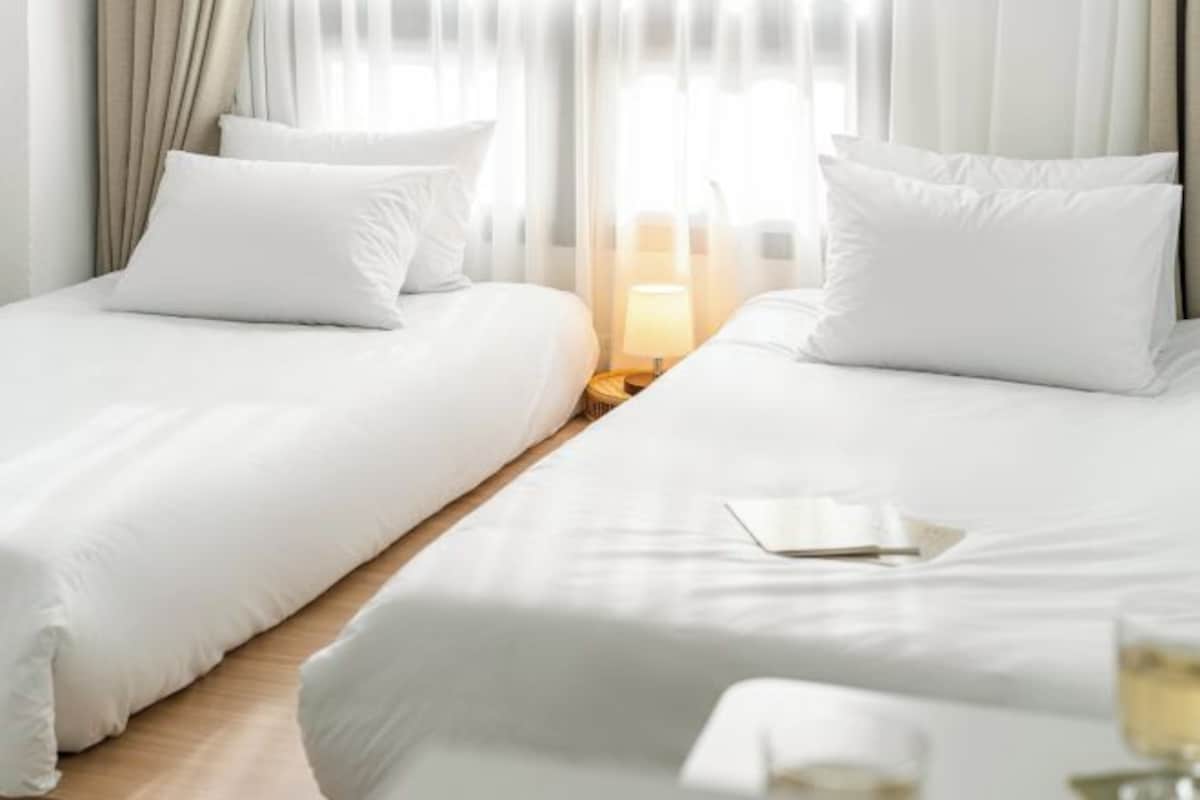 A hotel room with two beds, a bedside table with a lamp, and a window with curtains.