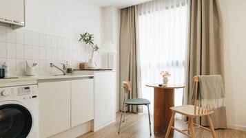 Cocina compacta con lavadora, comedor con mesa y sillas, y ventana con cortinas.