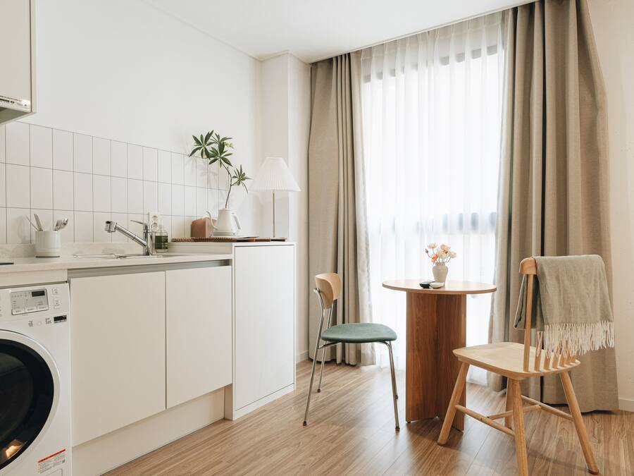 Cocina compacta con lavadora, comedor con mesa y sillas, y ventana con cortinas.