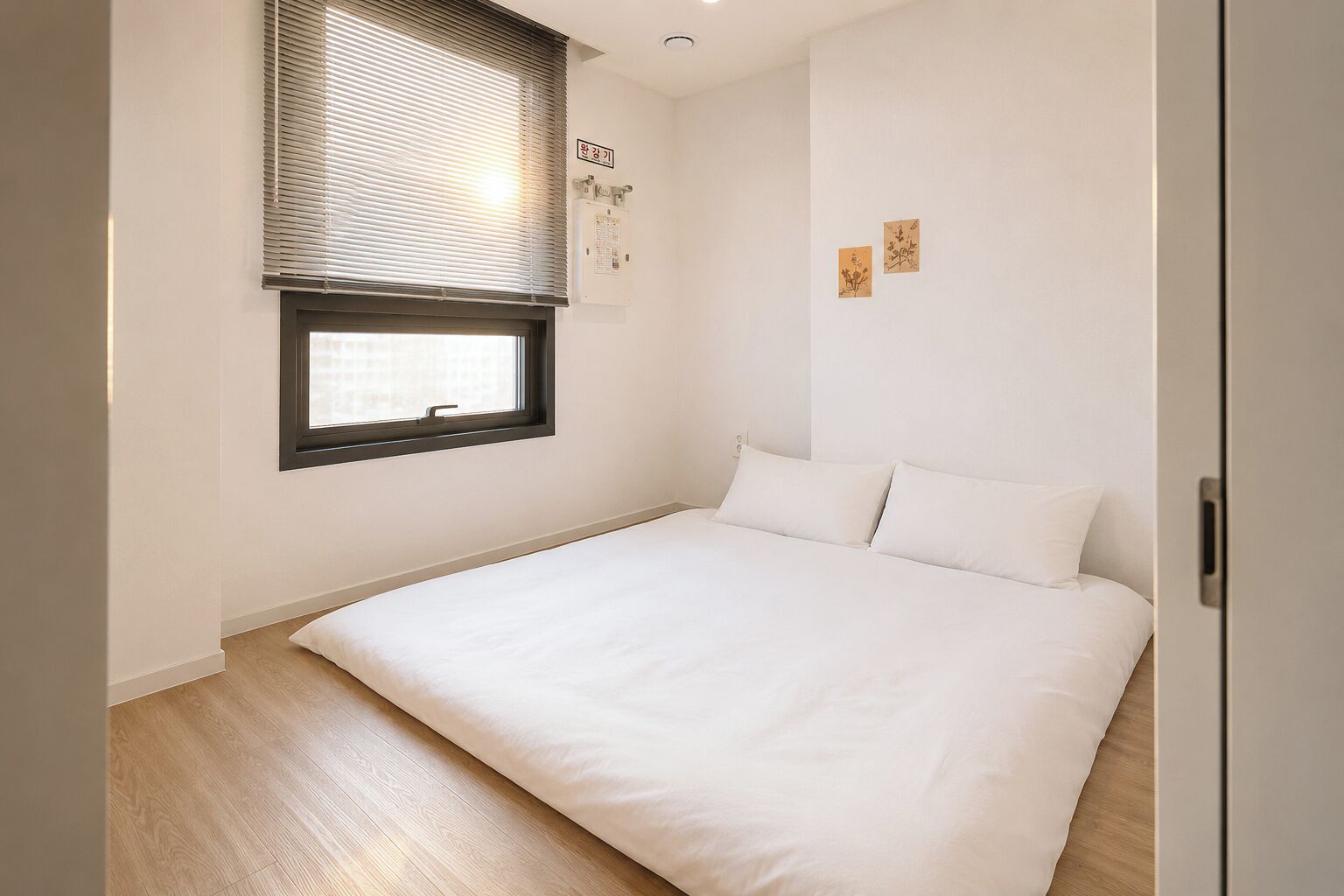 A bedroom with a bed, a window with blinds, a wall-mounted air conditioning unit, and a door.