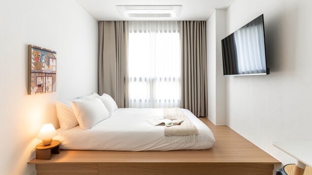 Habitación de hotel moderna con una cama grande, televisión de pantalla plana y ventana con cortinas.
