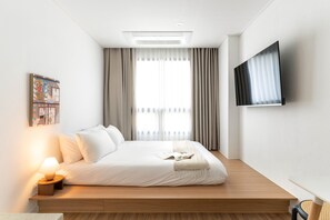 A modern hotel room with a large bed, a flat-screen TV, and a window with curtains.