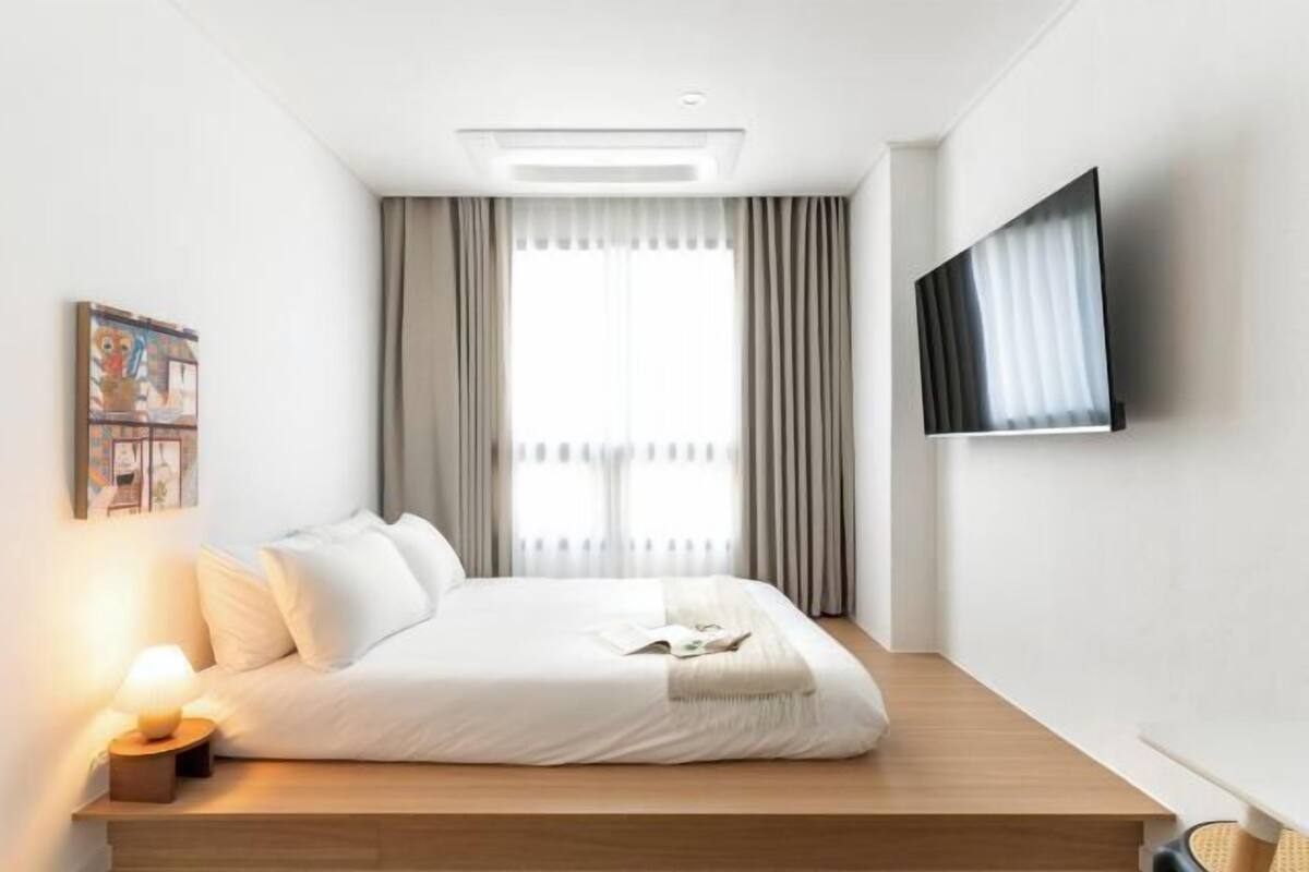 Una habitación de hotel moderna con cama, televisor de pantalla plana, lámpara de noche y ventana con cortinas.