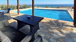 A covered outdoor area with a pool, stone flooring, wicker furniture, and a view of the sea. - Dreamy South Sea View Villa Residence with Pool - Upper Level (Frangokastello)