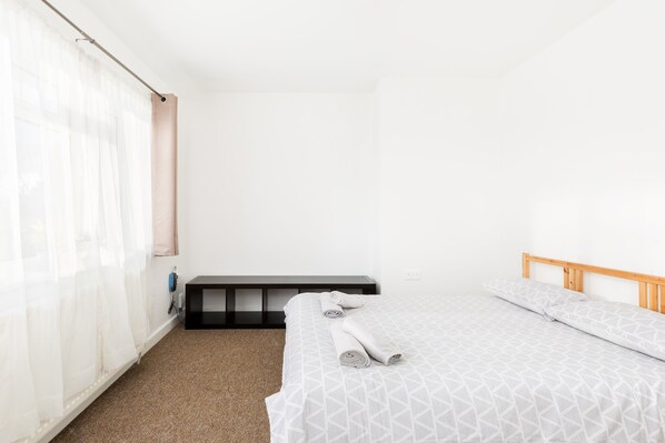 Une chambre d’hôtel avec un lit, un banc et une fenêtre ornée de rideaux légers.