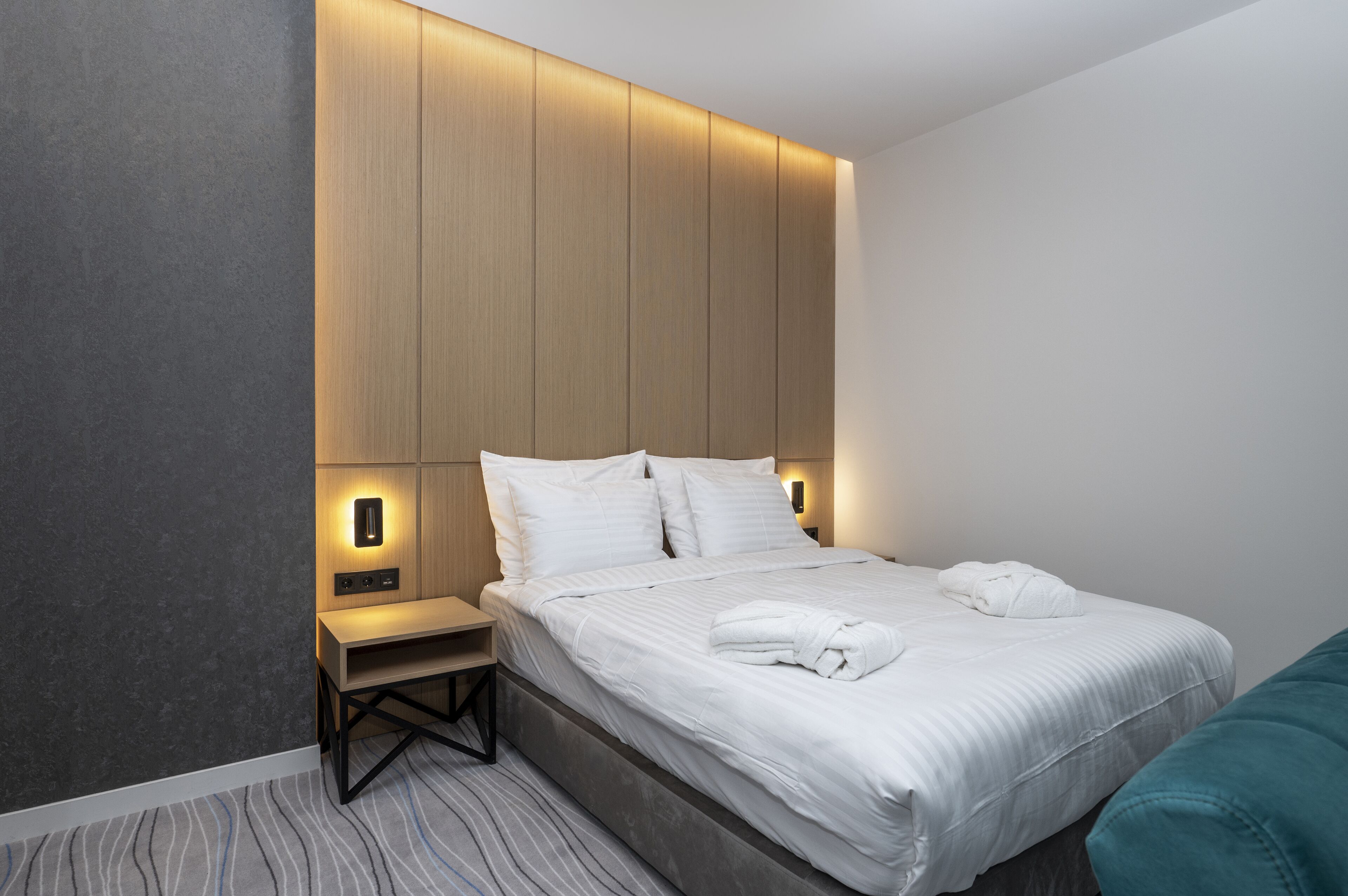 Una habitación de hotel moderna con una cama grande, mesitas de noche y cabecero incorporado.