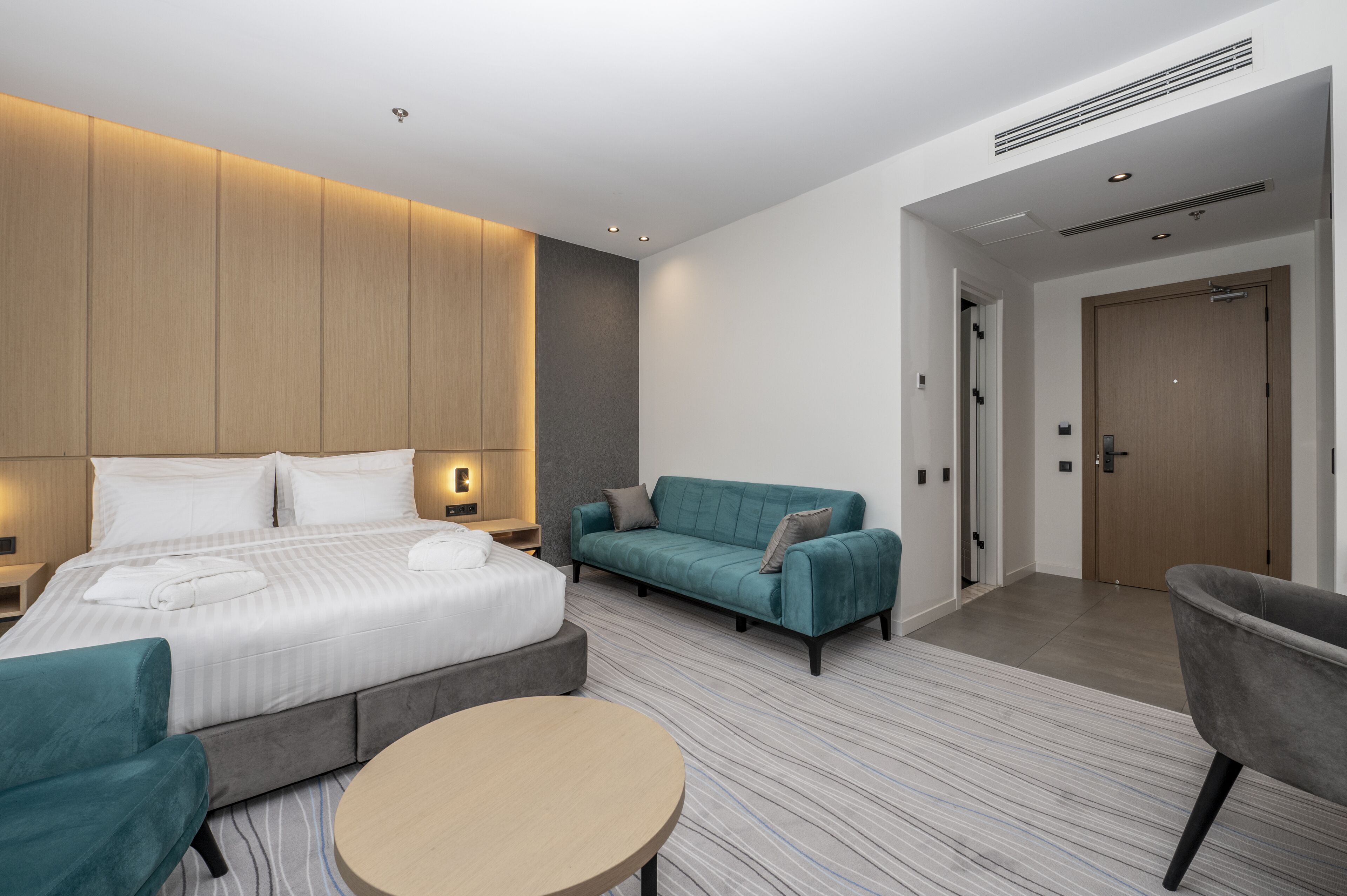 Una habitación de hotel moderna con una cama grande, un sofá, una mesa redonda y una puerta que da a otra habitación.