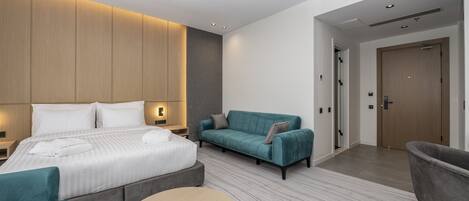 Una habitación de hotel moderna con una cama grande, un sofá, una mesa redonda y una puerta que da a otra habitación.