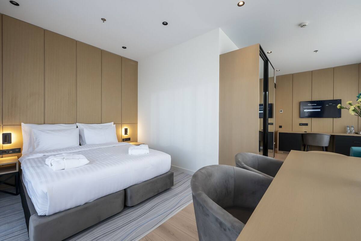 A modern hotel room with a large bed, bedside tables, a desk, and a flat-screen TV.