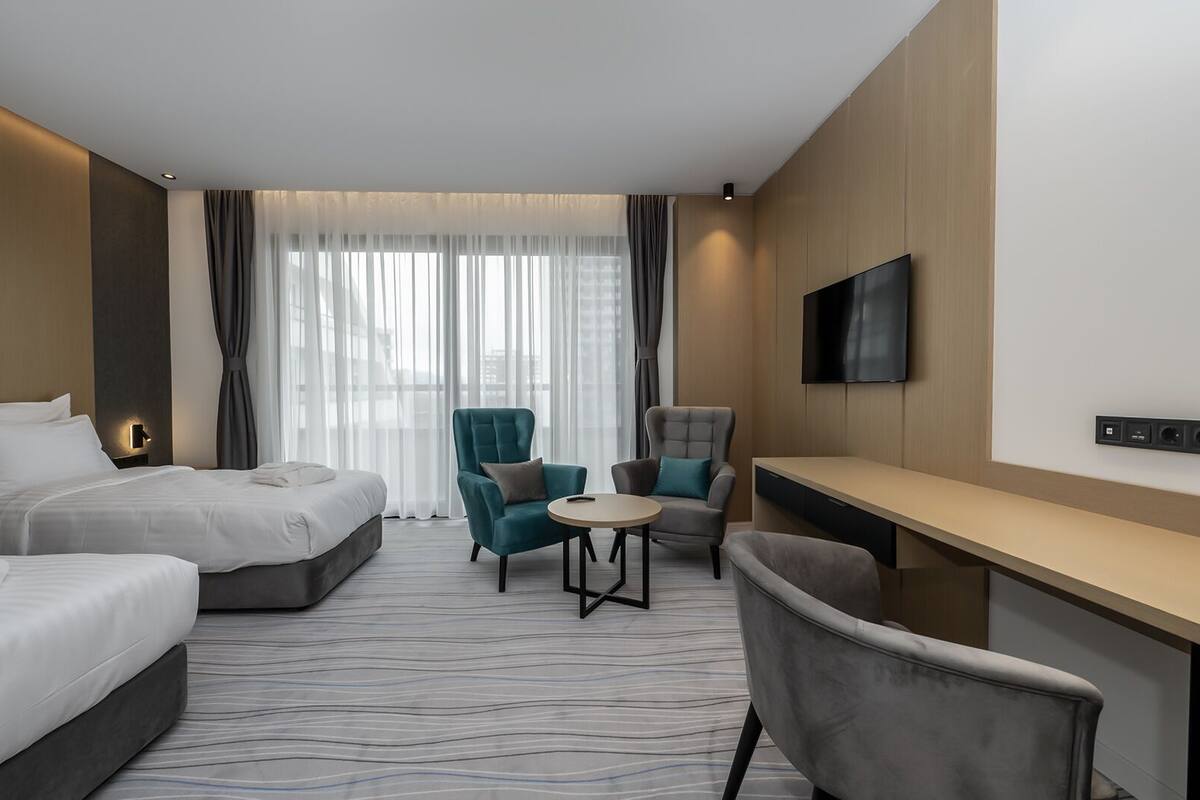 A hotel room with two beds, a desk, a TV, and a seating area with chairs.