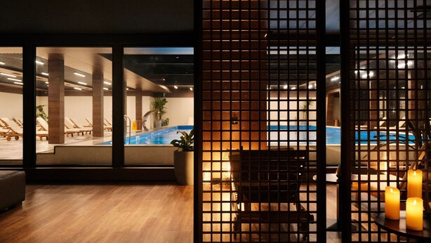 Habitación de hotel con vista a una piscina interior, piso de madera y una mampara con velas.