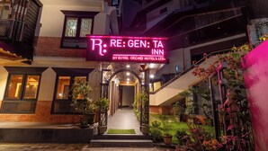 Entrada de hotel con letrero de neón, marquesina y plantas en macetas.