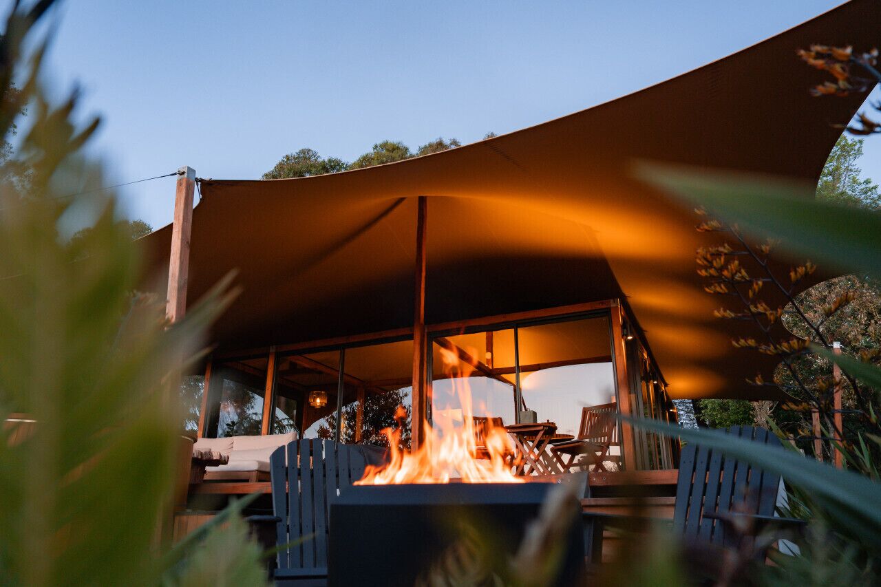 An outdoor seating area with a fire feature, wooden furniture, and a large canopy.