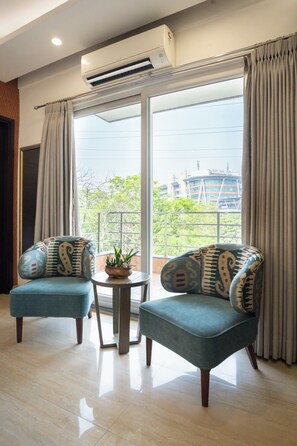 Ein Zimmer mit zwei blauen Sesseln, einem kleinen Tisch mit einer Pflanze und Blick auf Gebäude durch eine Glastür.