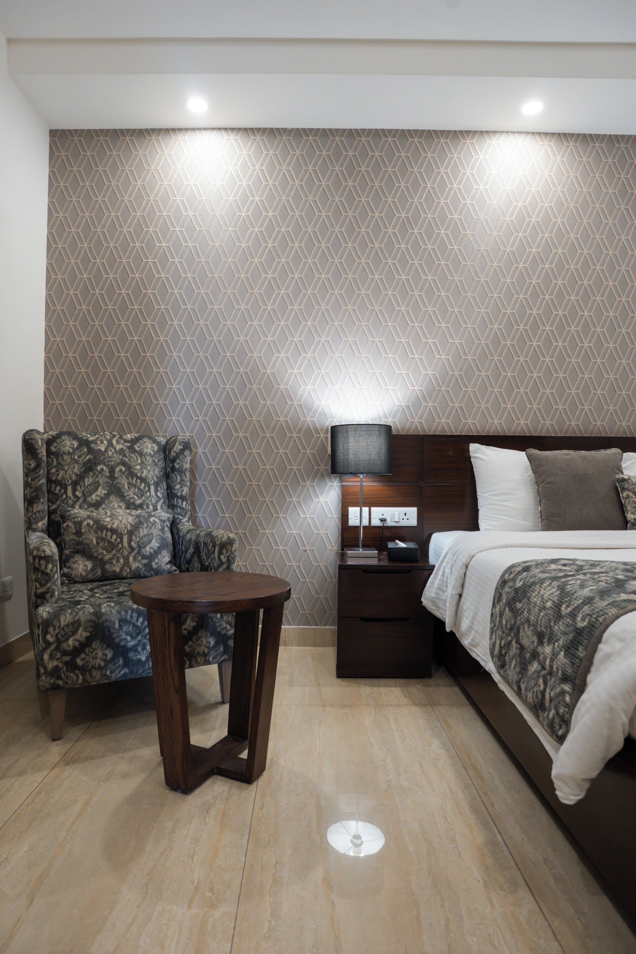 Une chambre à coucher avec un mur à motifs, un lit, une chaise, une table de chevet et une lampe.