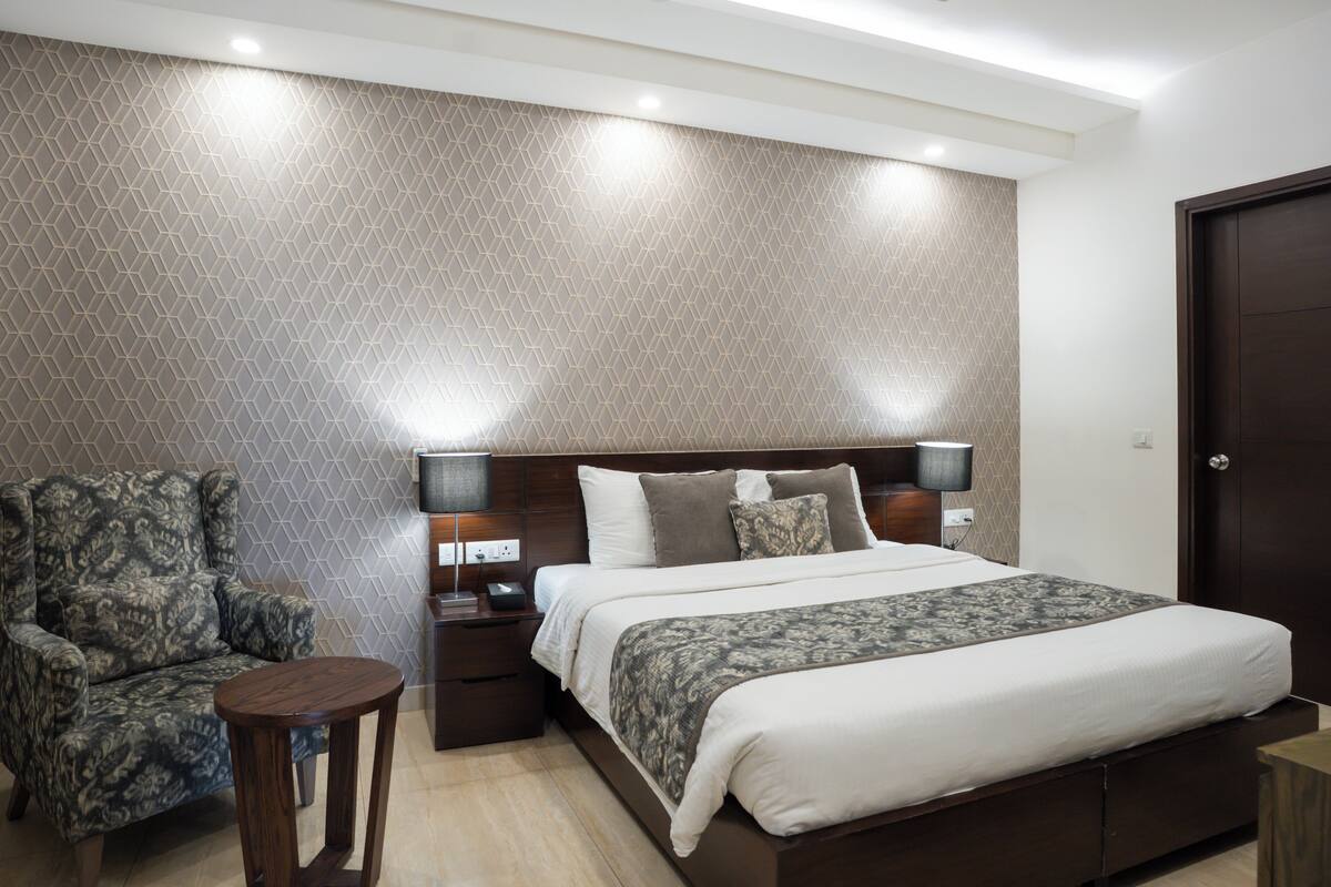 Ein Schlafzimmer mit Bett, Nachttisch, Lampe, Stuhl und einer Wand mit Muster.