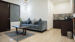 Un salon comprenant un canapé, une table basse, une plante, ainsi qu’un coin cuisine avec des placards et un évier.