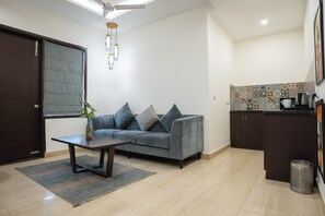 Ein Wohnzimmer mit einer Couch, einem Couchtisch, einer Pflanze und einer Küchenzeile mit Schränken und einem Spülbecken.