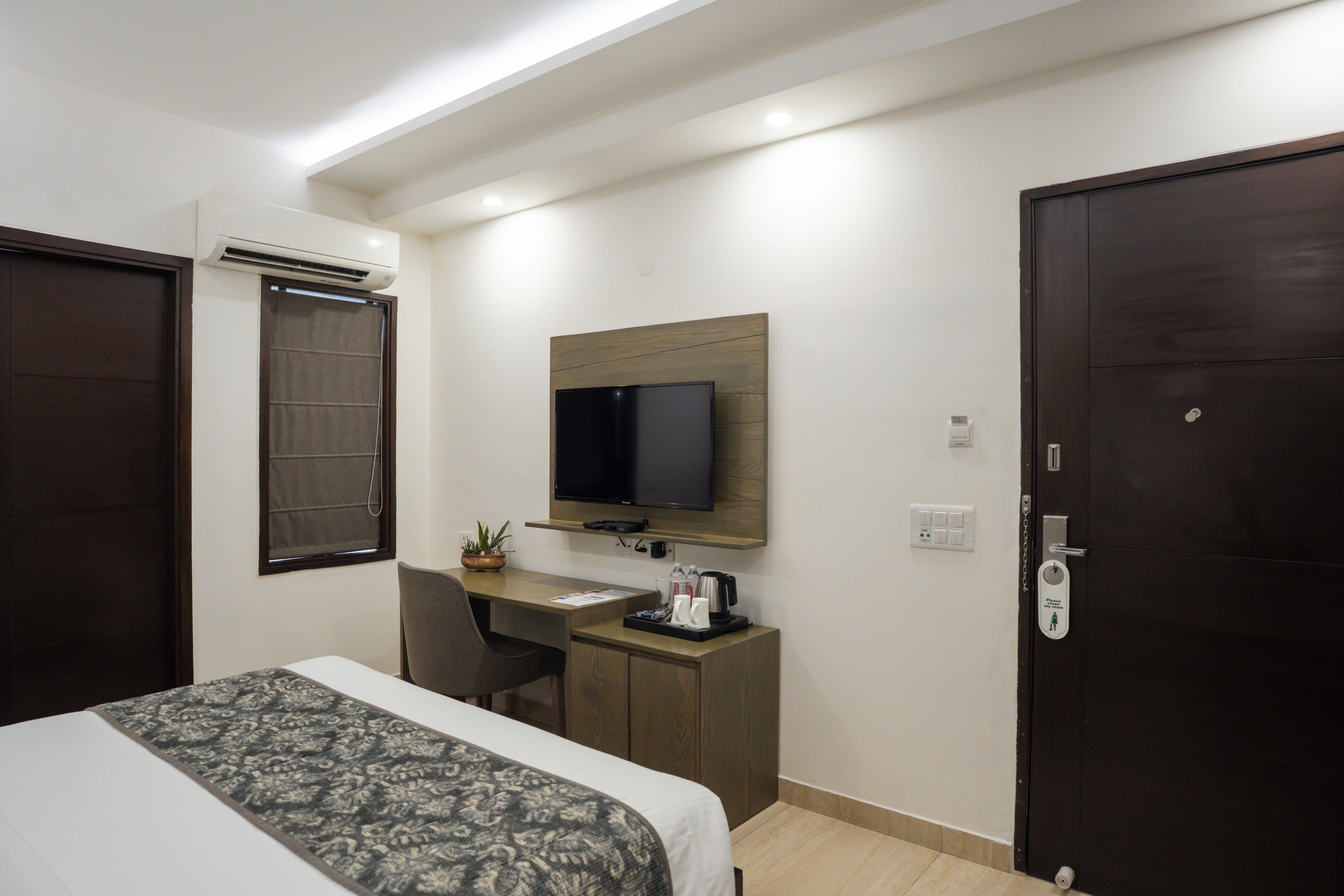 Una habitación de hotel con cama, escritorio, silla, televisor y puerta.