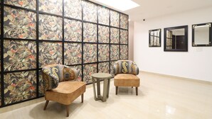 Une pièce comprenant deux fauteuils, une petite table ronde et un mur décoratif orné d’un motif floral. Trois miroirs sont accrochés au mur.