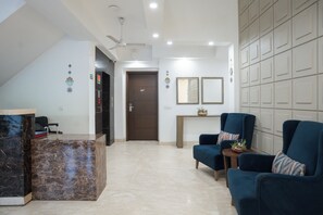 A modern living room with a marble reception desk, two blue armchairs, a ceiling fan, and a door marked '007'.
