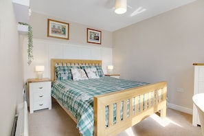 Quarto com cama de madeira, mesas de cabeceira brancas, um criado-mudo e radiador fixado na parede.