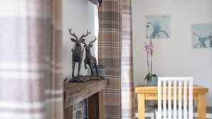 Een knus vertrek met een open haard, een houten tafel en een witte stoel.