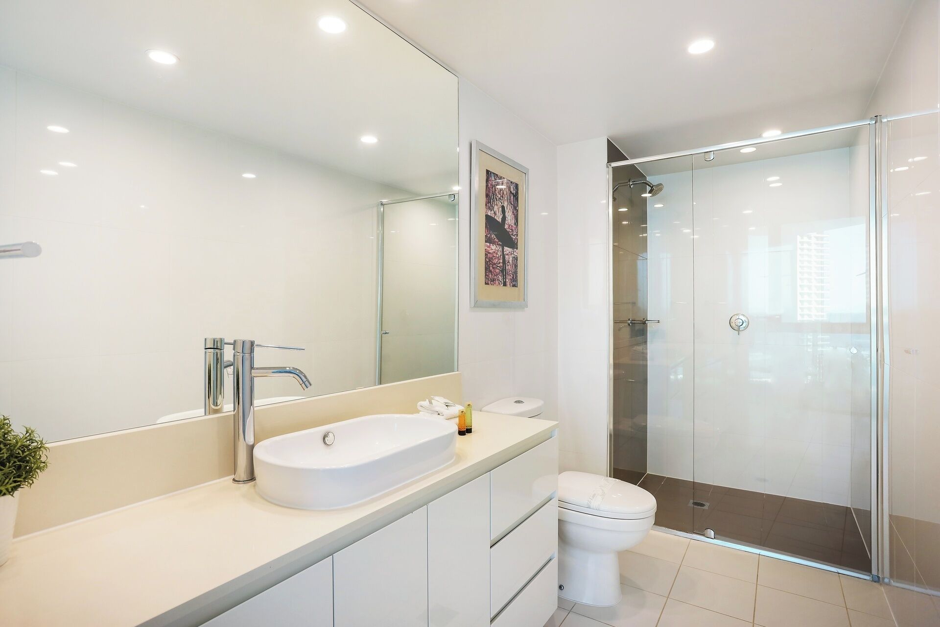 Un baño moderno con un espejo grande, un lavamanos blanco, un inodoro y una ducha con mampara de cristal.